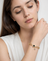 Woman wearing Aria Noir Charm Bracelet, gold-plated chain bracelet with black enamel charm and crystal detail for everyday elegance